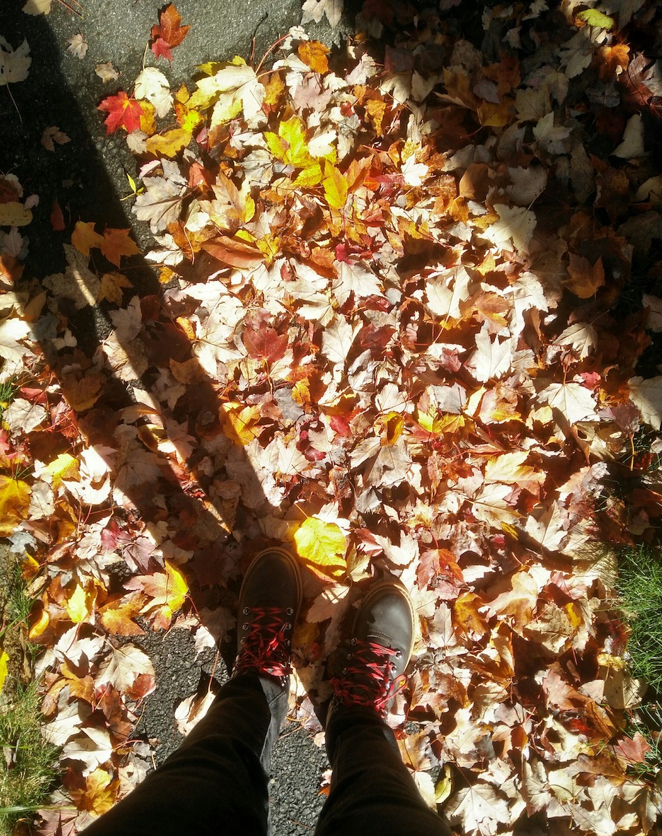 Black boots with red laces black pants standing on ground covered in fall leaves
